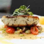 grilled sea bass with sauteed tomatoes served with potatoes ball on white plate