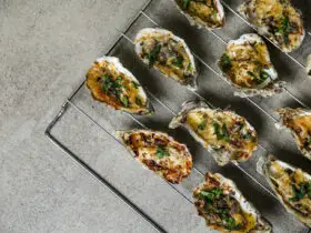 Cooling rack with tasty baked oysters on grey background